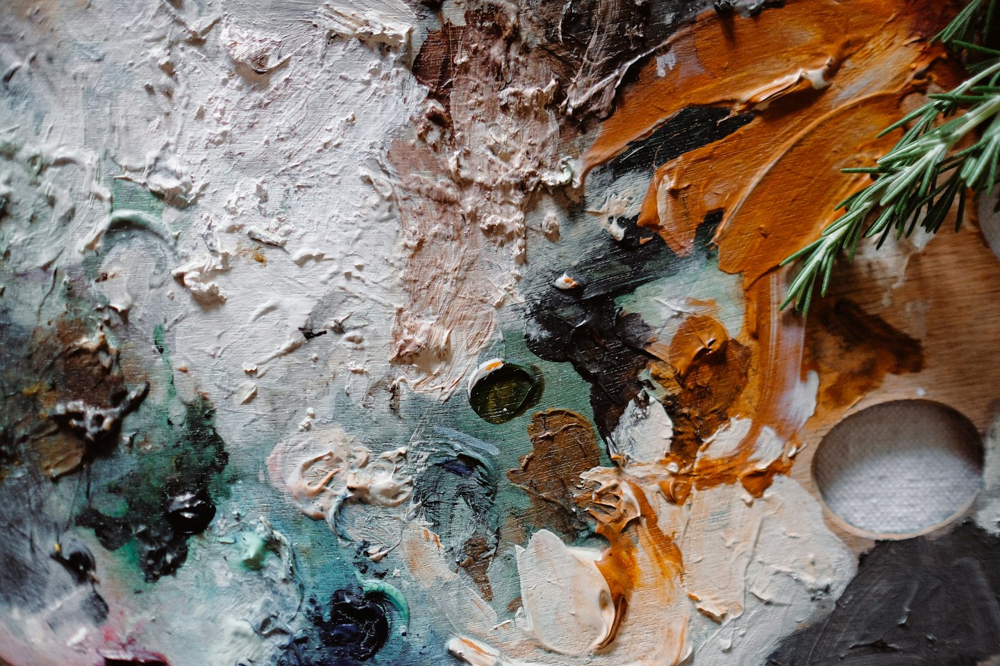 Tavolozza di un artista con oli colorati e rametto di rosmarino.