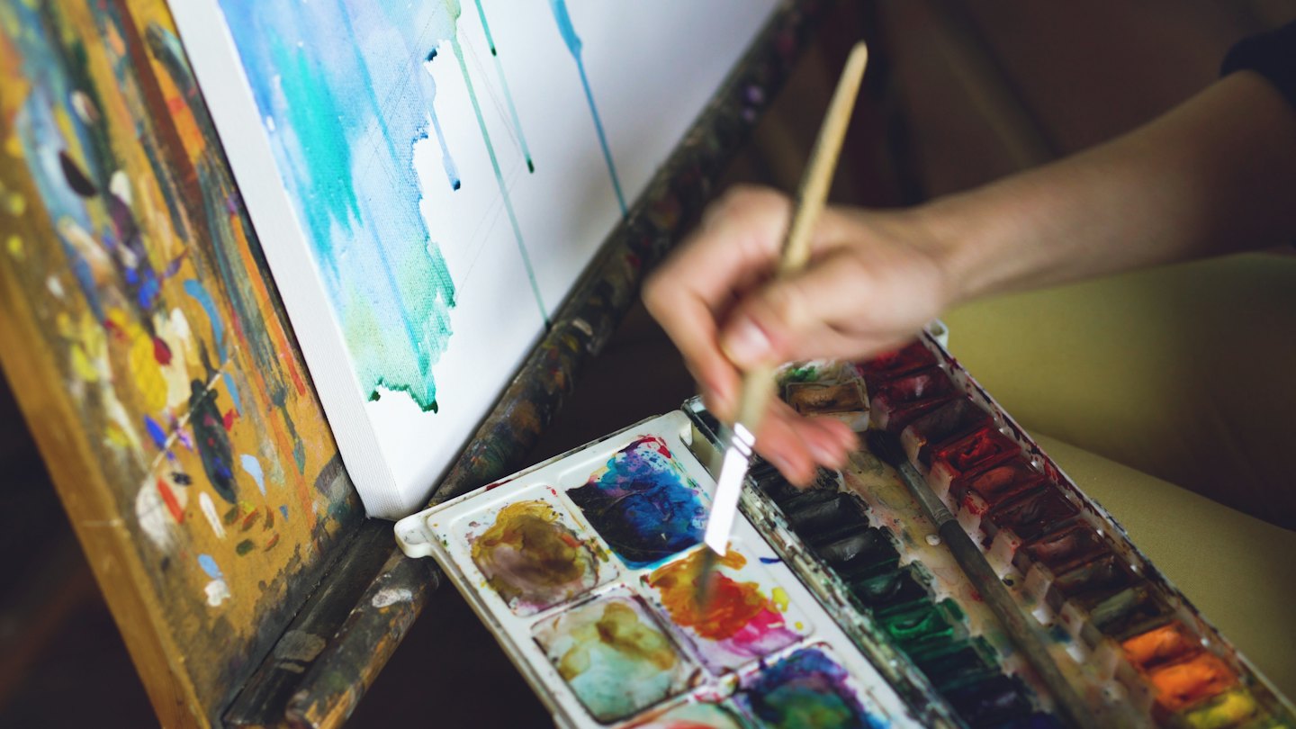 Mano di artista intinge un pennello in una tavolozza di acquerelli.